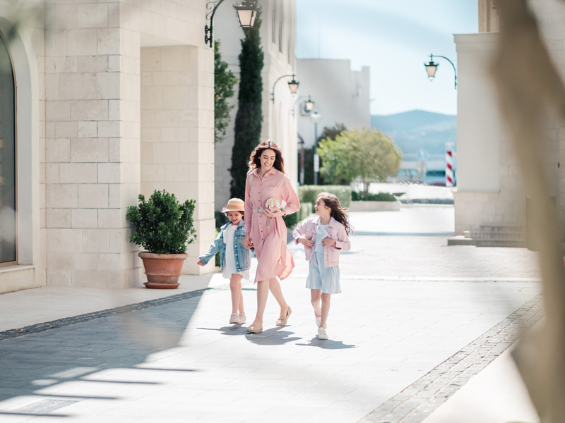 Mother walking with her two daughters in Porto Montenegro, wearing light spring outfits and smiling.