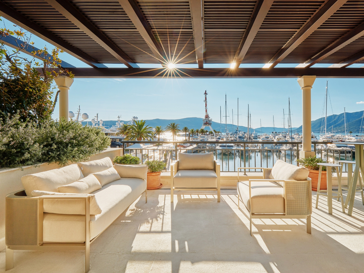 Luxury patio with comfortable seating overlooking a marina with yachts and mountains in the background.