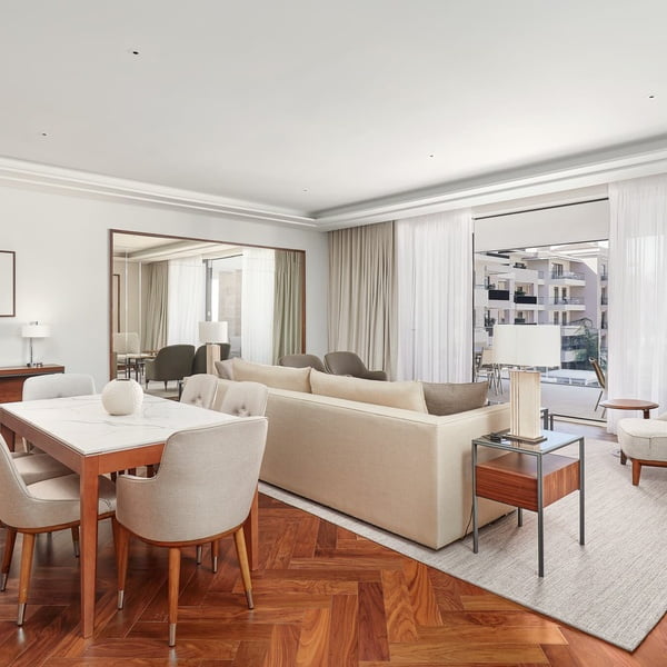 A sleek living room with a dining set, plush sofa, and floor-to-ceiling windows draped with sheer curtains, opens onto a balcony.