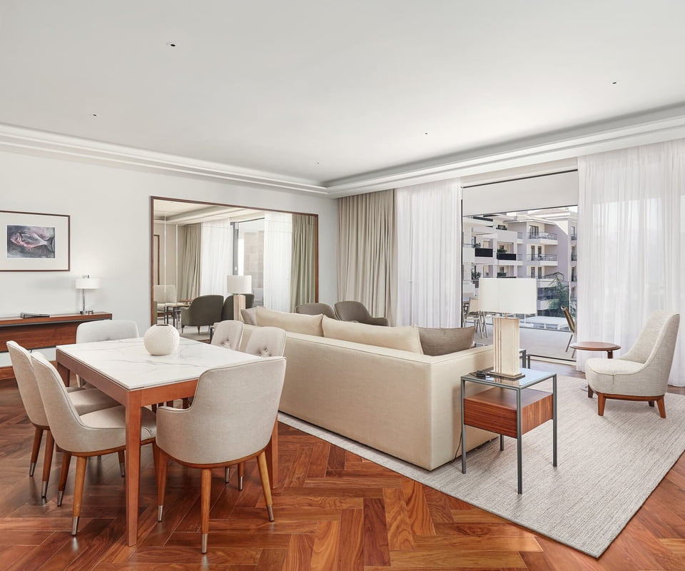 A sleek living room with a dining set, plush sofa, and floor-to-ceiling windows draped with sheer curtains, opens onto a balcony.
