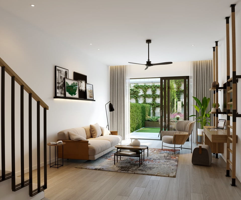 A contemporary living room with a beige couch, wooden furnishings, and artwork on the wall, opening up to a garden through glass doors.