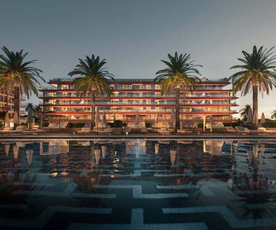 Luxurious resort facade at Porto Montenegro, featuring modern architecture with terraced levels, illuminated at dusk, complemented by a reflective pool and surrounded by tall palm trees enhancing the tropical ambiance.
