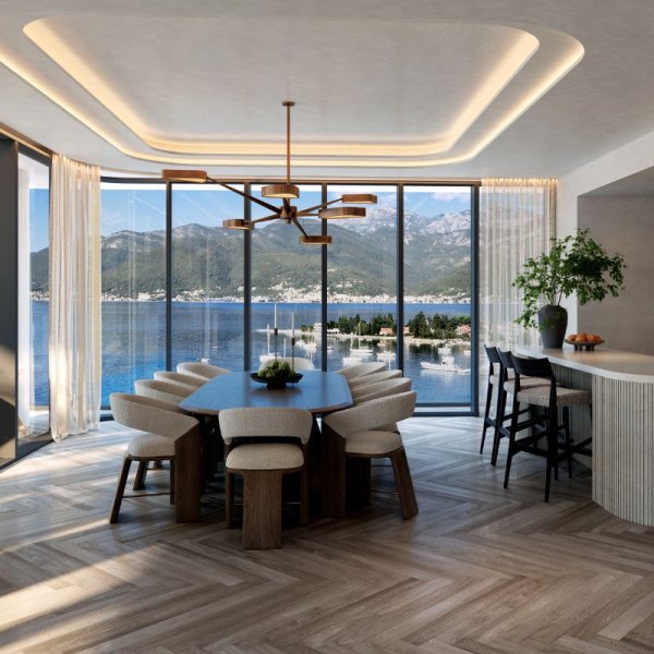 Spacious and elegantly designed dining and kitchen area in AERIS, Porto Montenegro, featuring modern furnishings, a stylish hanging light fixture, and large windows that provide breathtaking views of the bay and surrounding mountains.