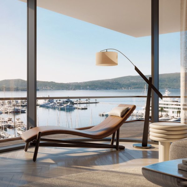 Relaxing lounge area in AERIS, Porto Montenegro, featuring a stylish reclining chair and floor lamp, with floor-to-ceiling windows offering a panoramic view of the bustling marina and serene sea landscape.