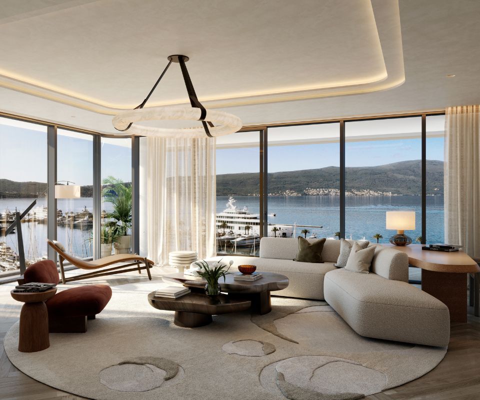 Spacious living room in Synchro Residences, Porto Montenegro, with elegant modern furnishings, floor-to-ceiling windows offering panoramic views of the marina and mountains, and sophisticated interior design that complements the scenic outdoor setting.