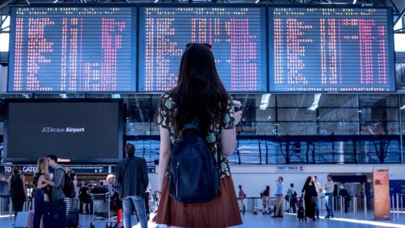 A woman at the airport in Montenegro, eagerly awaiting flight arrival times on the schedule board.