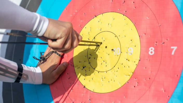 An archer's hand is removing arrows from the bullseye of an archery target.