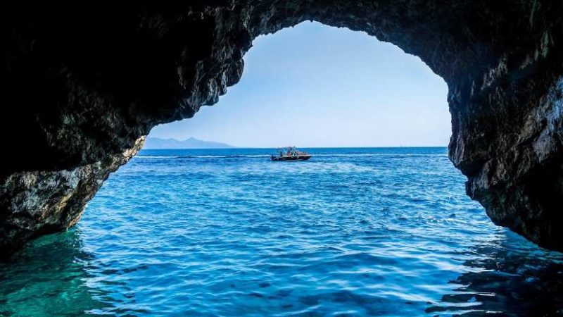 View from inside the Blue Cave in Montenegro, looking out toward the Adriatic Sea, with sunlight filtering through the narrow entrance, creating a mesmerizing blue glow in the water.