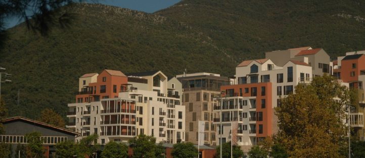 Picturesque neighborhood featuring modern residential buildings with a hillside backdrop. The scene captures lush greenery and a mix of architectural designs under a clear blue sky.