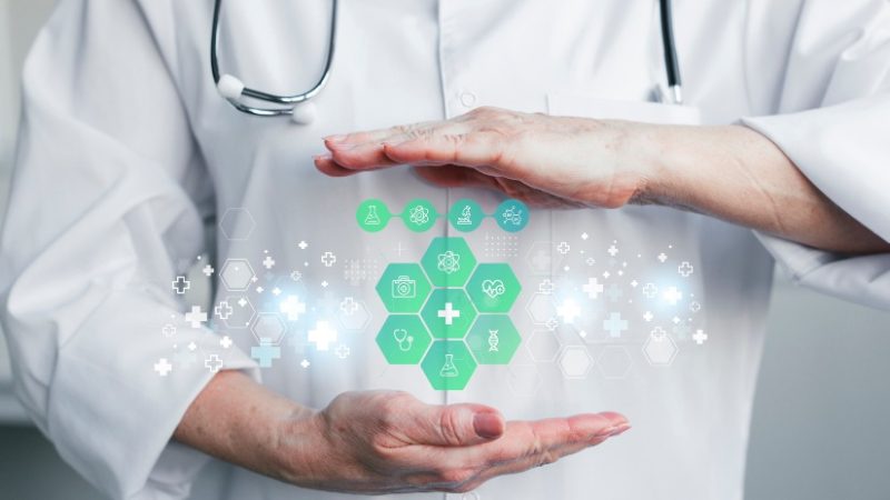 A doctor stands confidently, holding a green and white medical icon, symbolizing health and care in a professional setting.