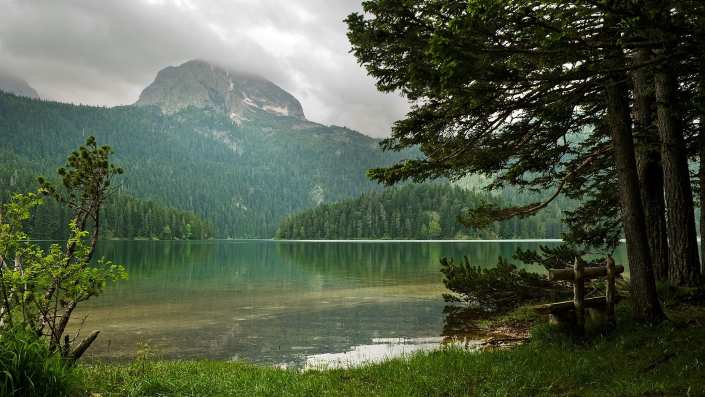 A stunning landscape of Durmitor National Park with a calm, clear lake surrounded by towering mountains and lush forests.