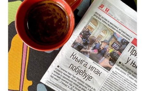 Kosmos Book picture featuring a newspaper with a Cyrillic headline, next to a red cup of coffee.