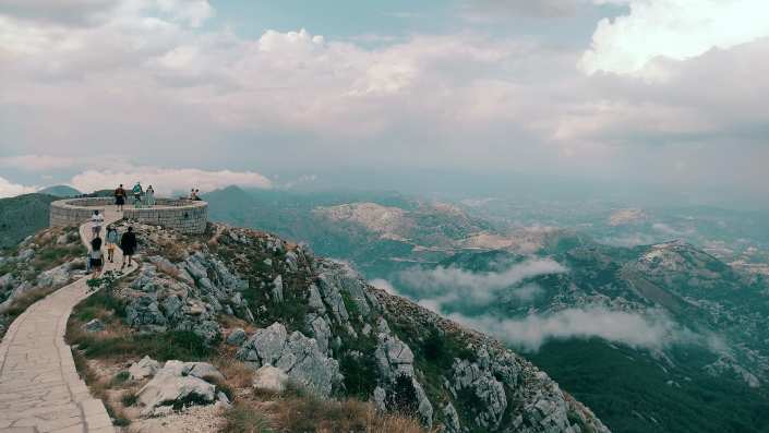 A breathtaking view from Lovćen National Park, featuring expansive mountains and a vibrant, green landscape under a cloudy sky.