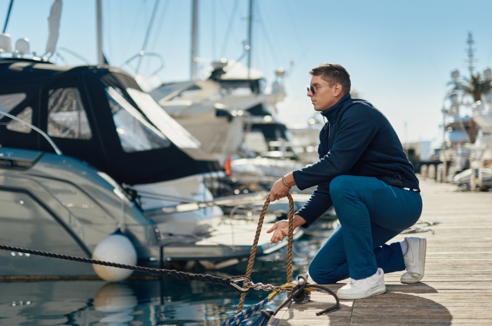 A man works diligently to dock a boat at a marina, dressed in a navy outfit and sunglasses, highlighting teamwork in nautical settings.
