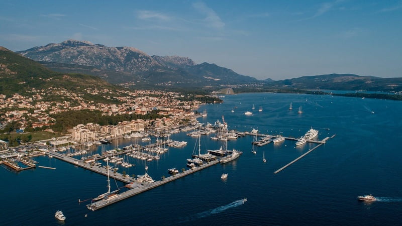 Aerial view of Marina village, Porto Montenegro with boats docked, surrounded by majestic mountains in the background.
