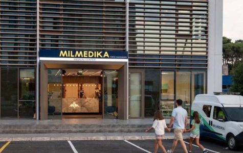 A modern medical center with a sign reading "MILMEDIKA Medical Center Porto Montenegro." The entrance has glass doors and a sleek interior with a marble reception desk. A man and two young girls walk towards the clinic, while a medical vehicle is parked nearby.