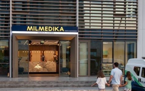 A modern medical center with a sign reading "MILMEDIKA Medical Center Porto Montenegro." The entrance has glass doors and a sleek interior with a marble reception desk. A man and two young girls walk towards the clinic, while a medical vehicle is parked nearby.