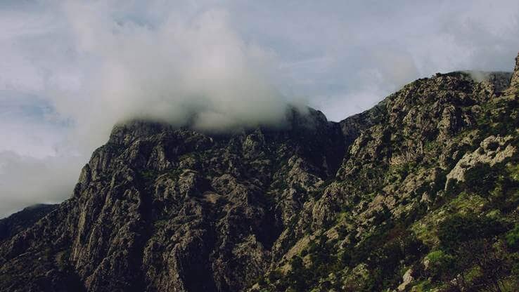 Rugged mountain peaks shrouded by low-hanging clouds, evoking a dramatic and moody atmosphere.