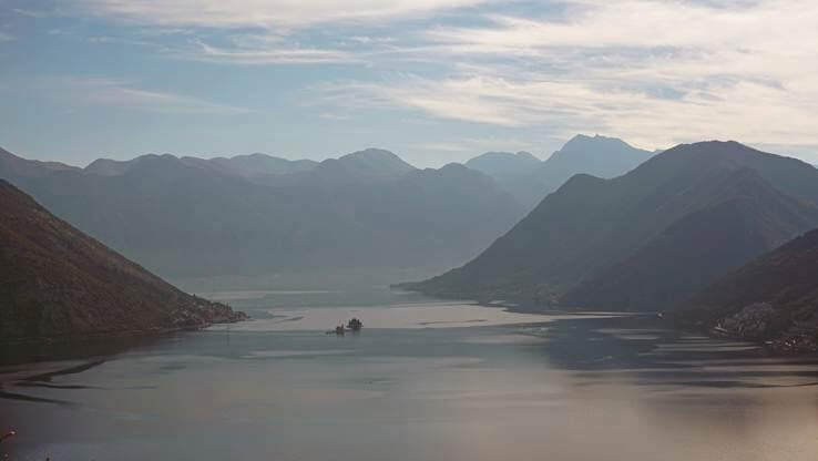 A tranquil scene of a vast lake flanked by layers of mountain ranges, bathed in soft light that enhances the ethereal beauty of the landscape.