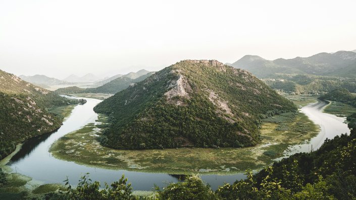 A serene river meanders through a lush green valley, framed by majestic mountains in the background.