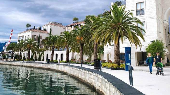 A picturesque scene along the Tivat Promenade, showcasing the vibrant boardwalk, lush greenery, and calm waters of the bay