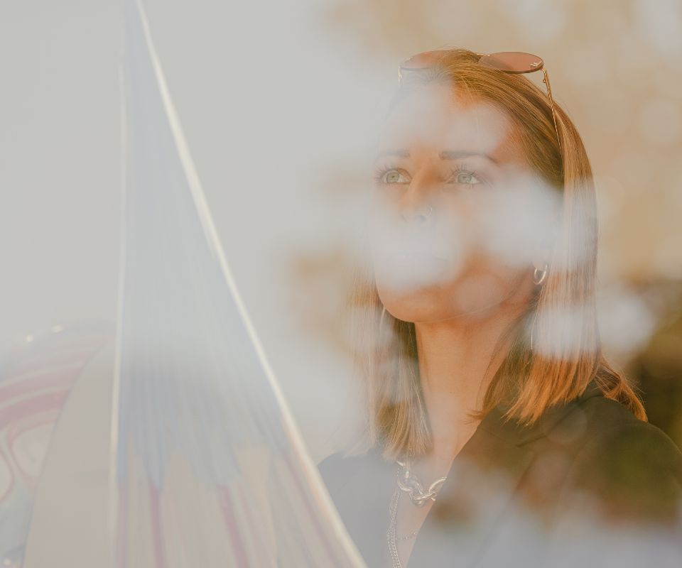 Artistic portrait of a woman thoughtfully gazing through a transparent glass sculpture, with a blurred marina background subtly reflecting in the glass, creating a serene and introspective mood.