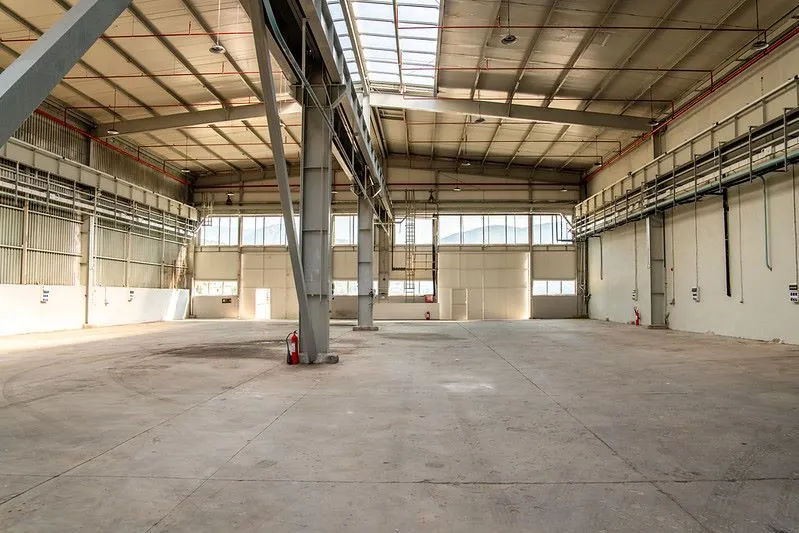 A spacious, empty industrial hangar at Adriatic 42 shipyard with a high ceiling, concrete floors, and large steel beams supporting the structure.