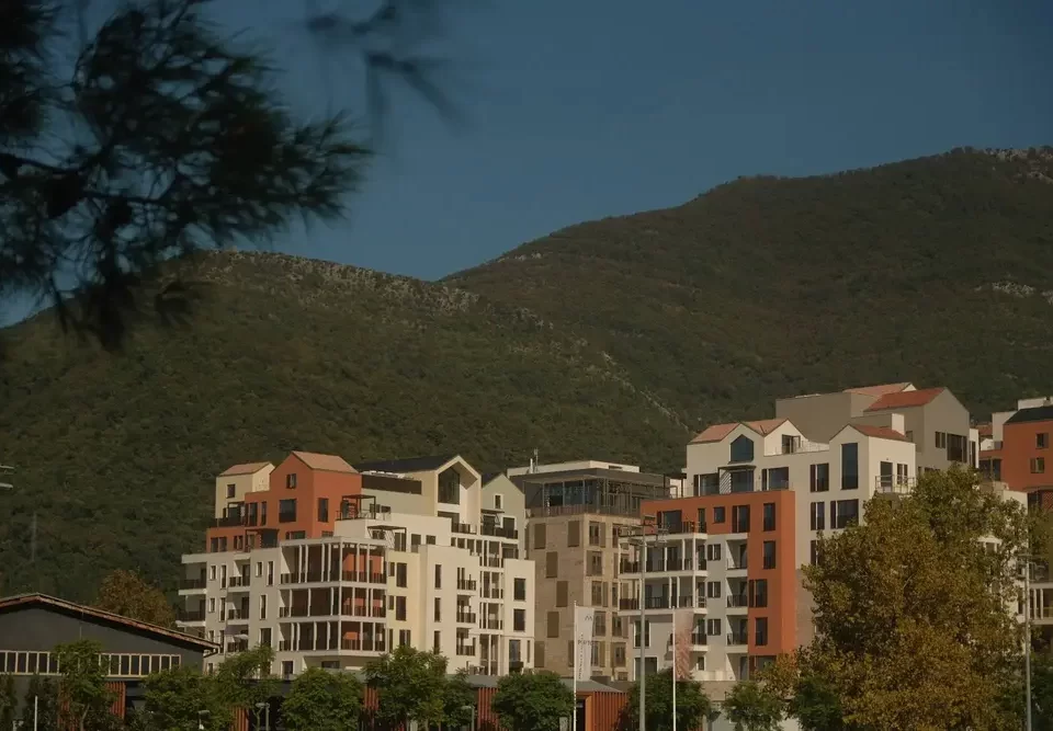 Picturesque neighborhood featuring modern residential buildings with a hillside backdrop. The scene captures lush greenery and a mix of architectural designs under a clear blue sky.