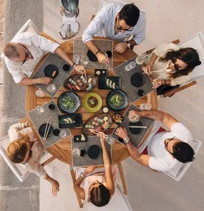 A group of friends enjoying a stylish outdoor dining experience at Porto Montenegro, sharing sushi and drinks around a beautifully set wooden table with an elegant marina ambiance.
