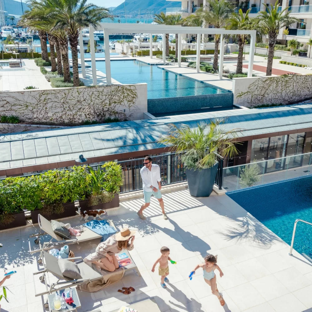 Family enjoying time by the pool in Porto Montenegro, with children playing and adults relaxing on lounge chairs.