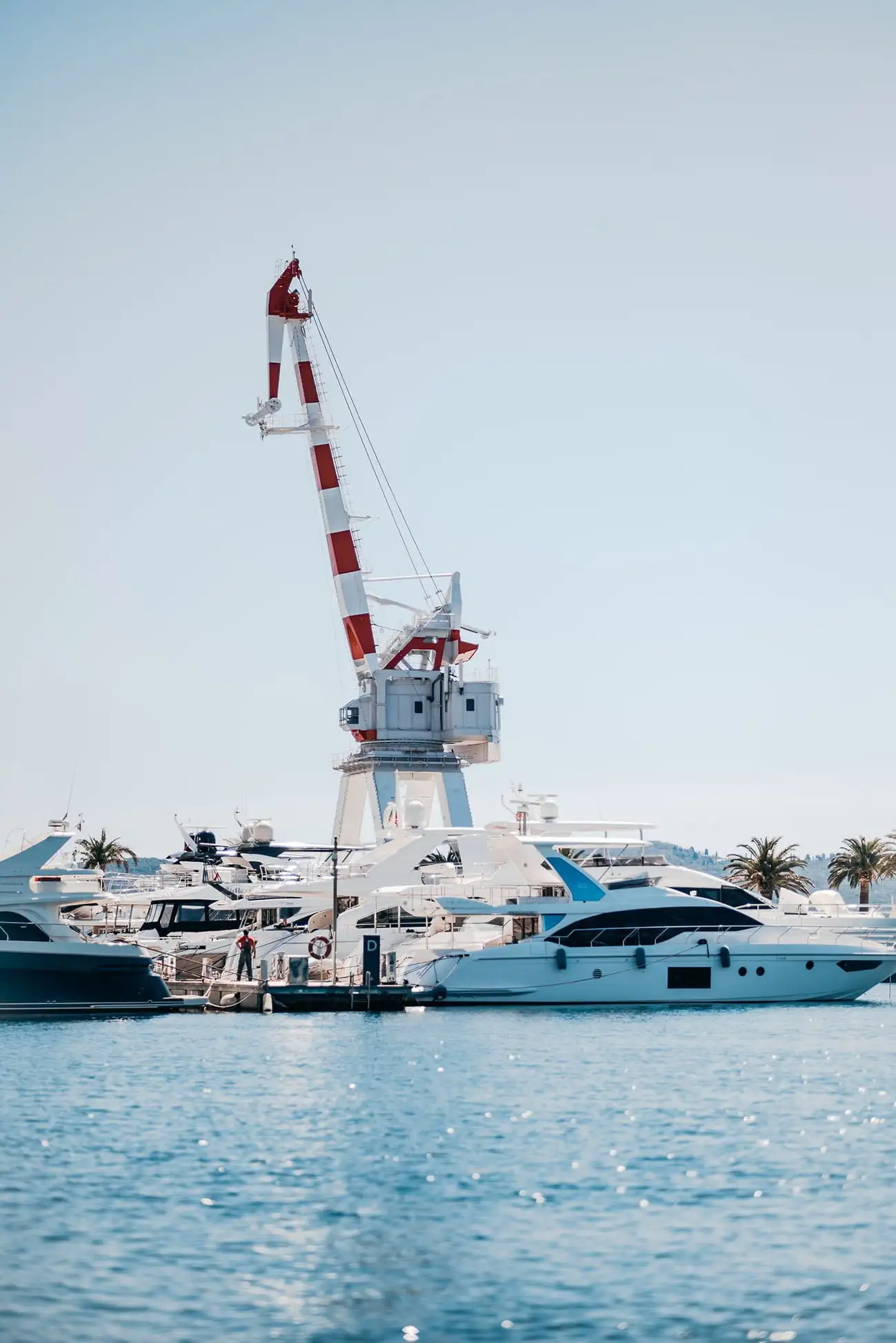 A striking red and white striped crane towering over luxurious yachts at Porto Montenegro Marina, symbolizing the area's rich maritime heritage and modern nautical lifestyle.
