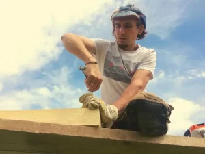 Portrait of Konstantin Evdokimov wearing a knit cap, working on a wooden structure outdoors.