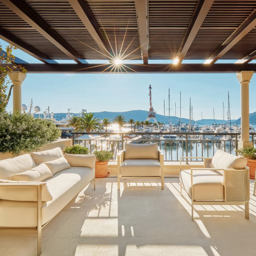 Luxury patio with comfortable seating overlooking a marina with yachts and mountains in the background.