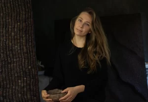 Portrait of Mila Halizova holding a stone sculpture, seated against a dark background.