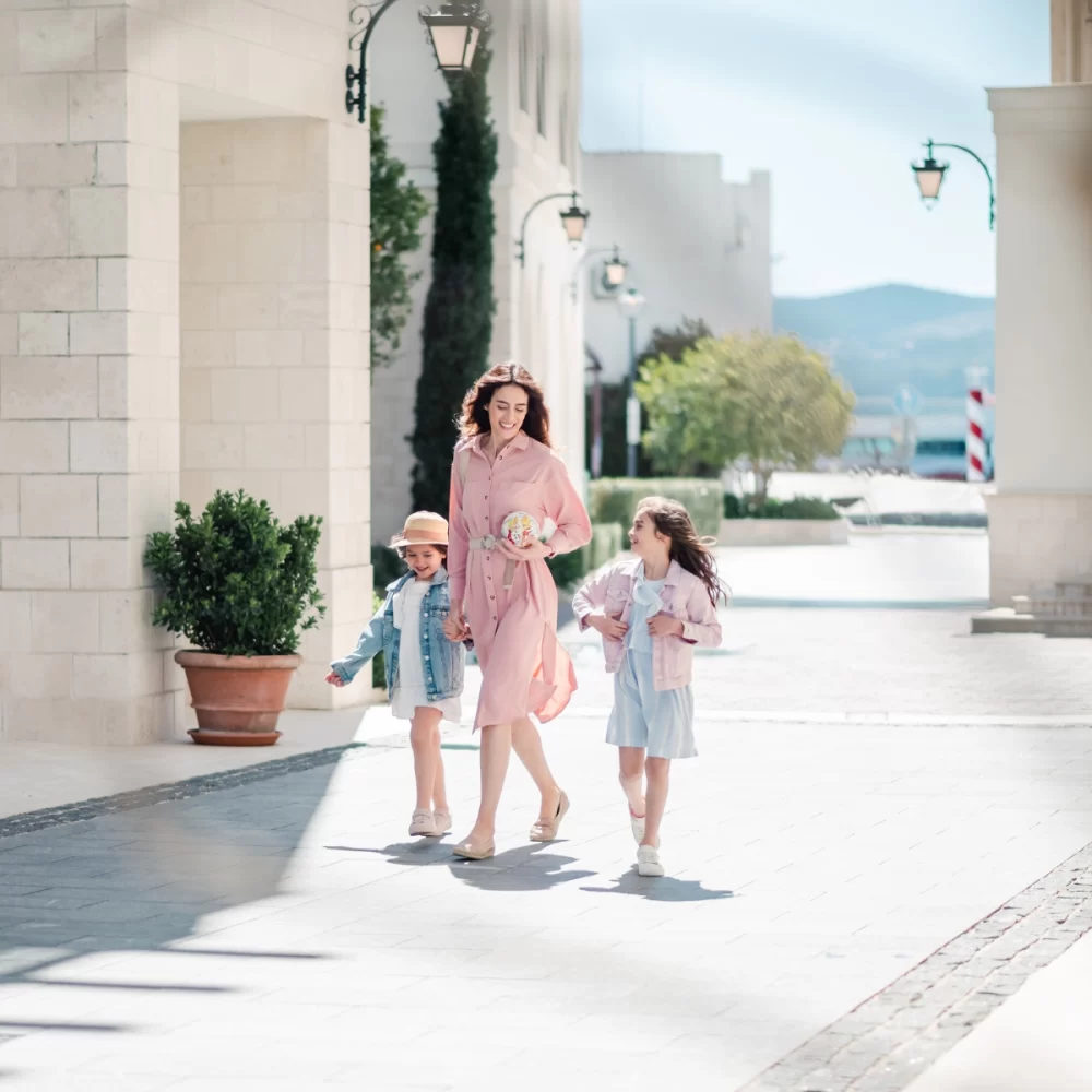 Mother walking with her two daughters in Porto Montenegro, wearing light spring outfits and smiling.