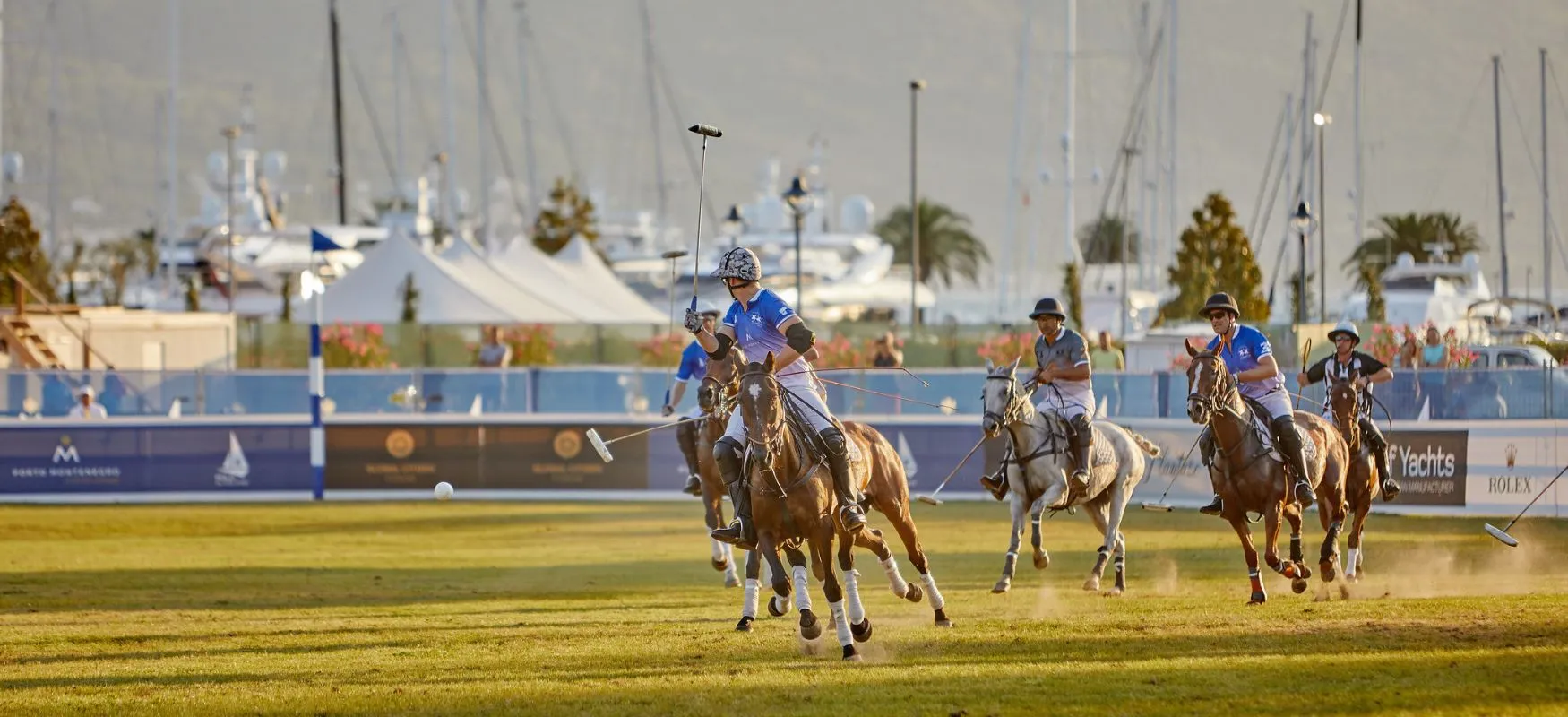 Action-packed polo match in Porto Montenegro with players on horseback chasing the ball, set against a backdrop of luxury yachts and marina, highlighting the blend of sport and high-end lifestyle.