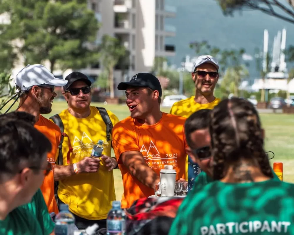 A group of participants in vibrant orange, yellow, and green shirts engaging in a lively outdoor event at Porto Montenegro, with a relaxed and cheerful atmosphere under the sun.