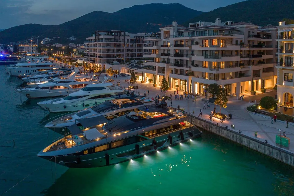 Porto Montenegro Marina at night, illuminated by warm lights from waterfront residences and yachts, creating a vibrant evening atmosphere along the marina promenade.