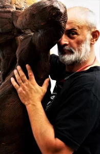 Portrait of Rajko Susic embracing a large wooden sculpture.