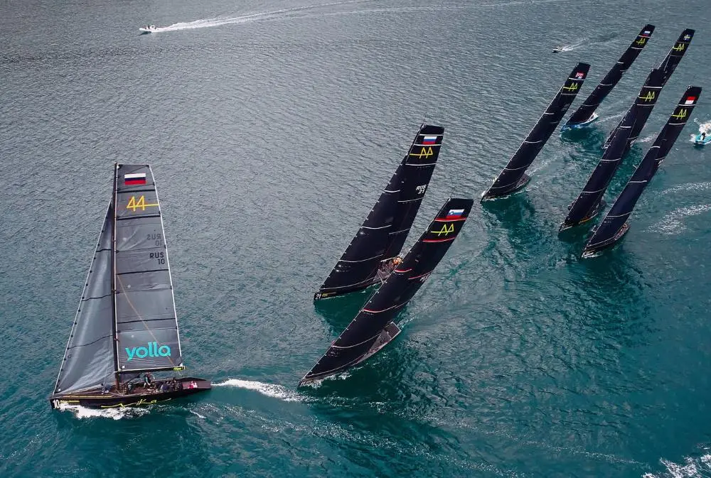An aerial view of a competitive regatta at Porto Montenegro, featuring sleek black sailboats racing across the deep blue waters, creating dynamic movement and energy on the sea.