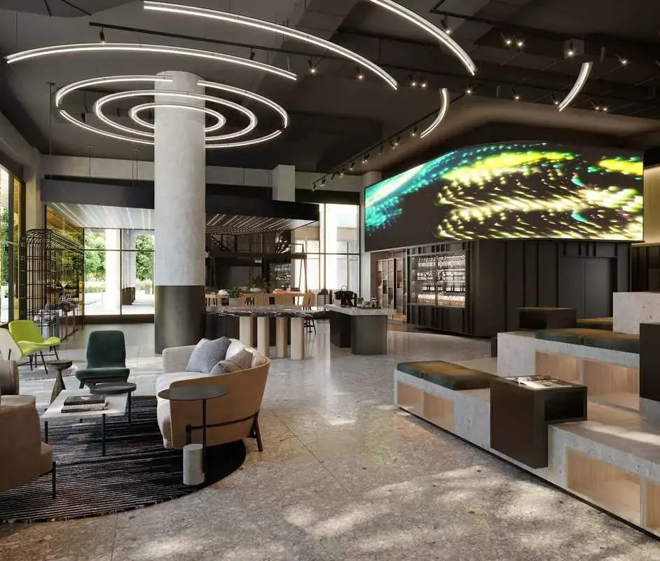 A modern hotel lobby with stylish furniture, artistic lighting fixtures, and a vibrant LED display, bathed in natural light.