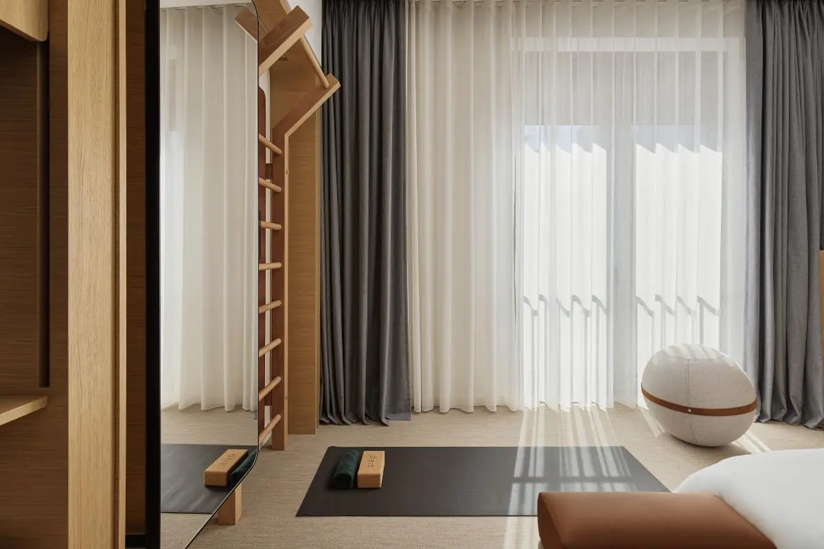 Peaceful yoga space with a minimalist design, featuring a yoga mat, wooden balance blocks, and a natural wood wall ladder. Large windows with sheer curtains allow natural light to fill the room.