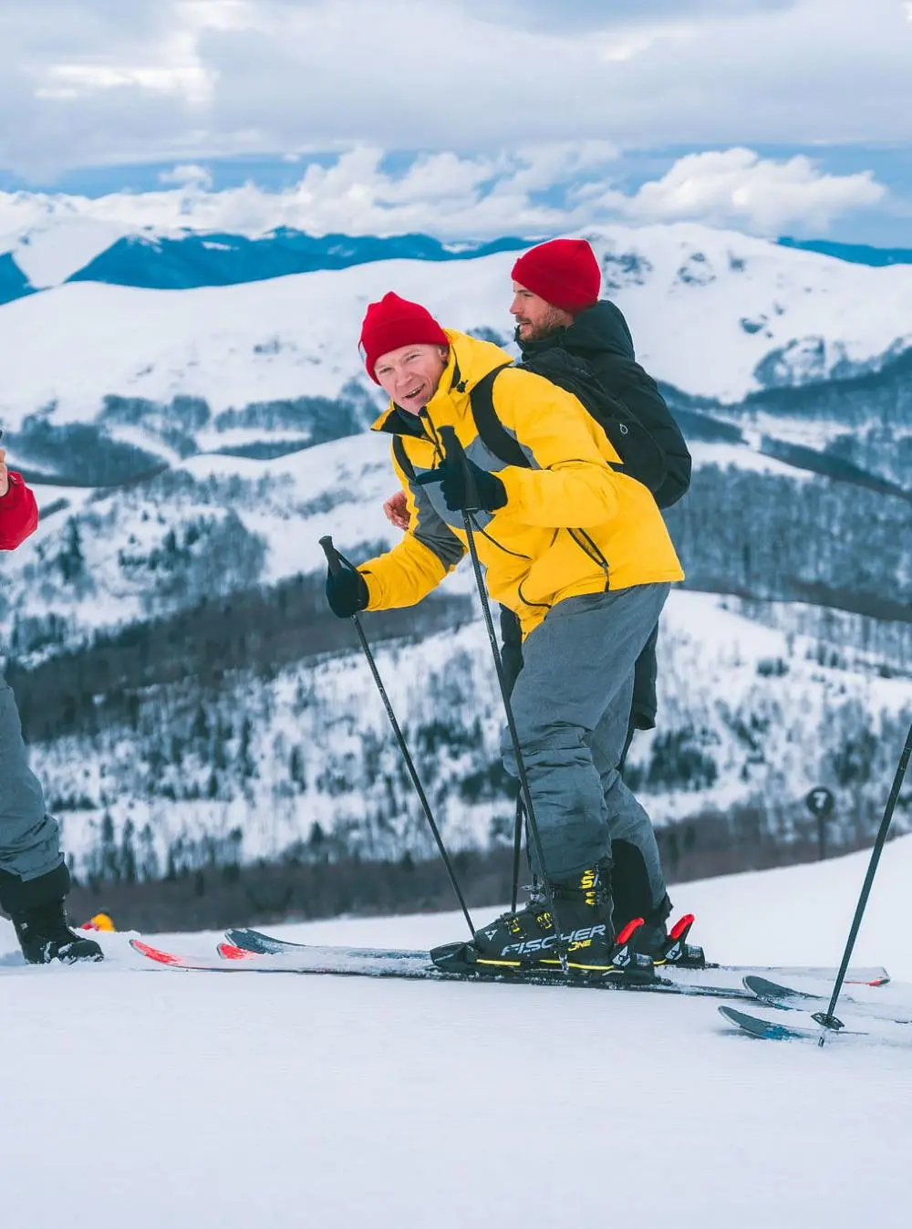 Two men dressed in warm ski gear, with one in a bright yellow jacket and a red beanie, enjoying a skiing adventure in the snow-covered mountains as part of a Crew Club winter excursion.