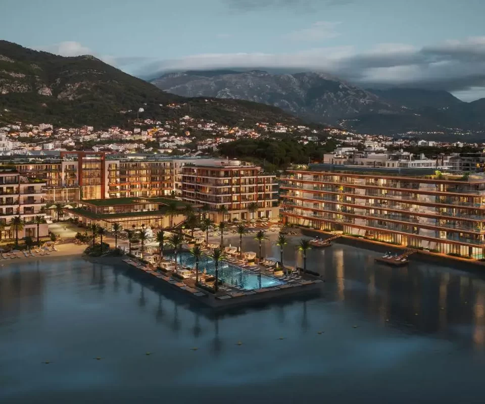 Night view of Synchro Yards, showcasing the illuminated AERIS residence with waterfront reflections and a mountain backdrop.